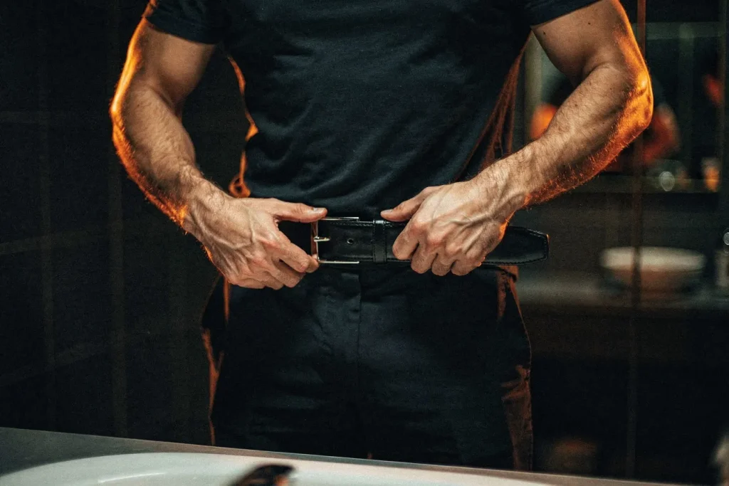 Man tightening his belt a notch, a sign of fat loss from consistent training
